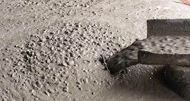 Frischer, noch sehr flüssiger Beton wird aus einem Rohr auf eine Baustelle gegossen. Die Oberfläche ist glänzend und zeigt deutliche Wasseranteile sowie grobe Gesteinskörnung.

                                    